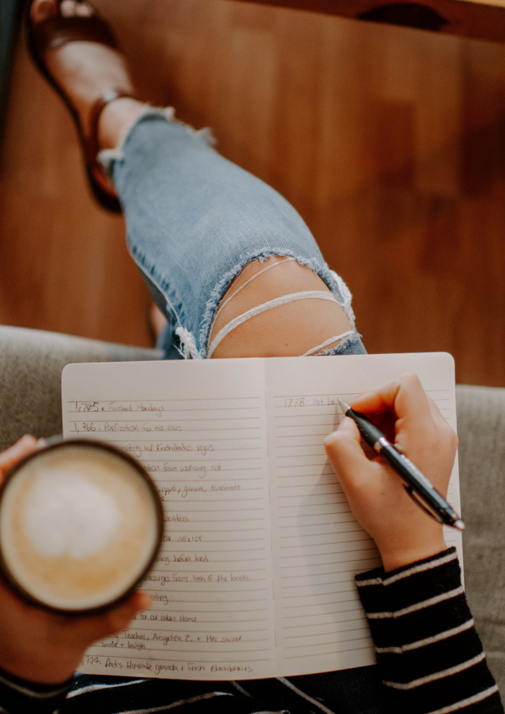 Person sitting with a warm cup of coffee and an open journal, writing thoughtfully, surrounded by a calm and inviting atmosphere perfect for reflection.