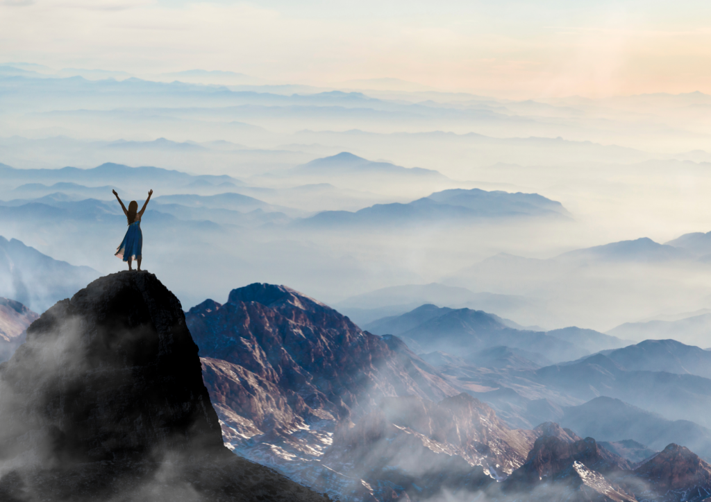 Woman standing on a mountain peak with her arms spread wide, embracing the freedom and vastness of nature, symbolizing release, empowerment, and the joy of letting go.